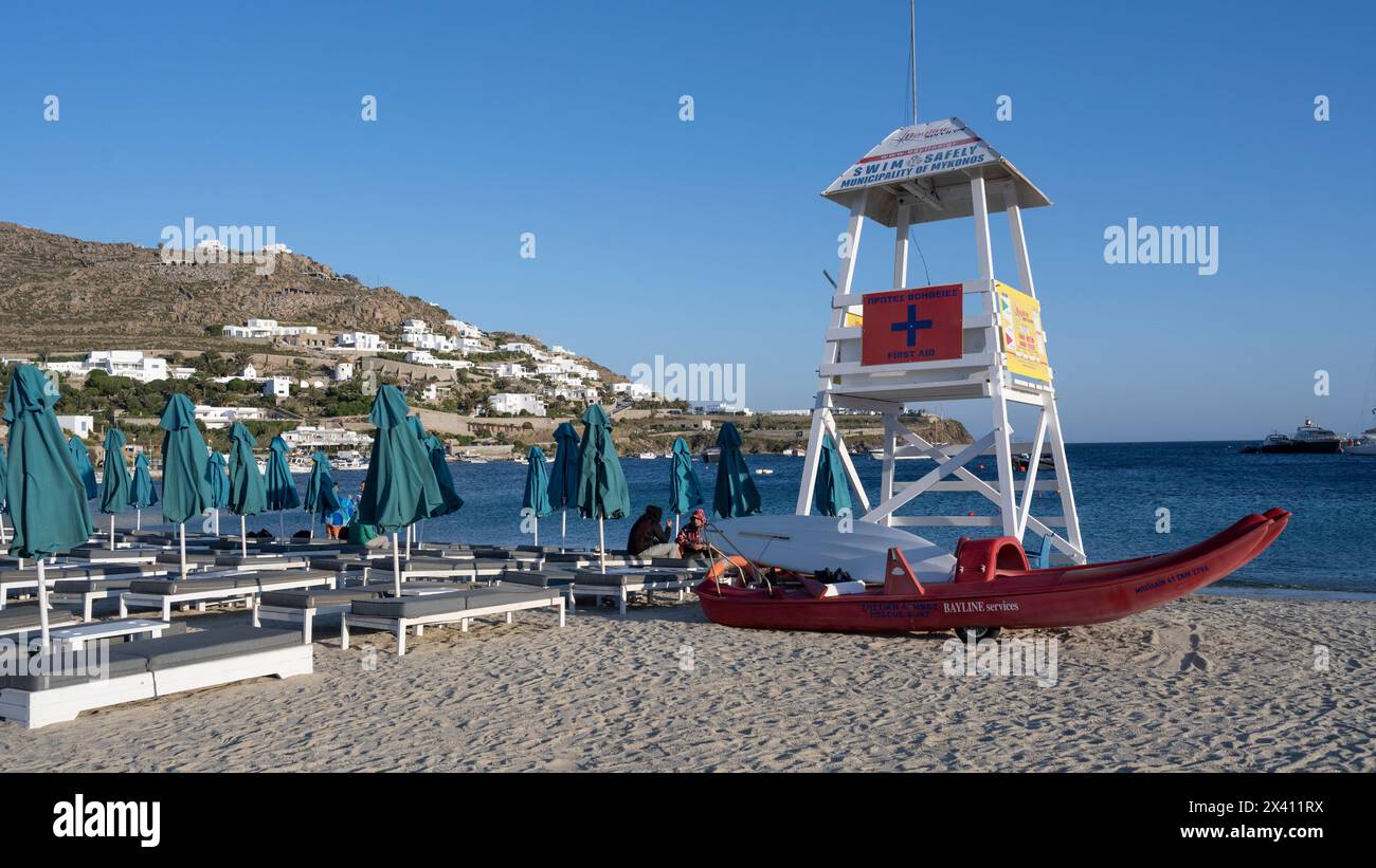 Stazione bagnino e posti a sedere con ombrelloni su una spiaggia dell'isola di Mykonos; Mykonos, Egeo meridionale, Grecia Foto Stock