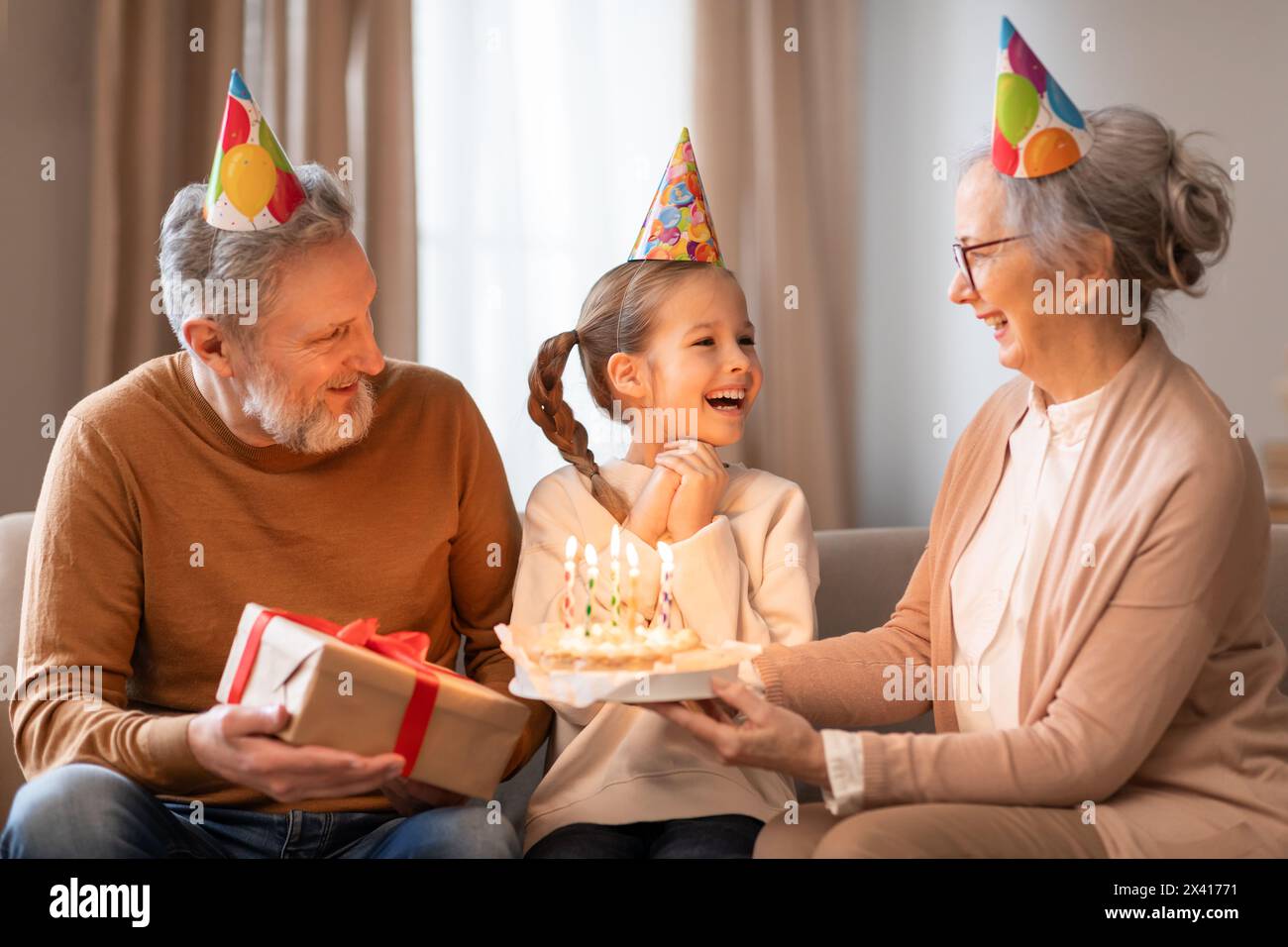 I nonni celebrano il compleanno delle loro nipoti in un accogliente soggiorno Foto Stock