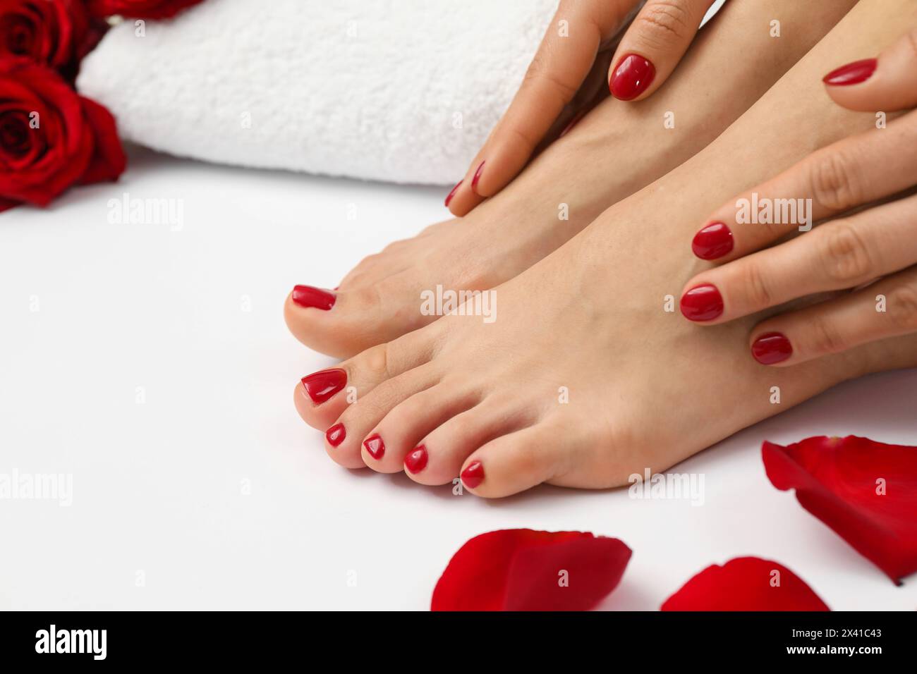 Donna con eleganti unghie rosse dopo la procedura di pedicure e petali di rosa su sfondo bianco, primo piano Foto Stock