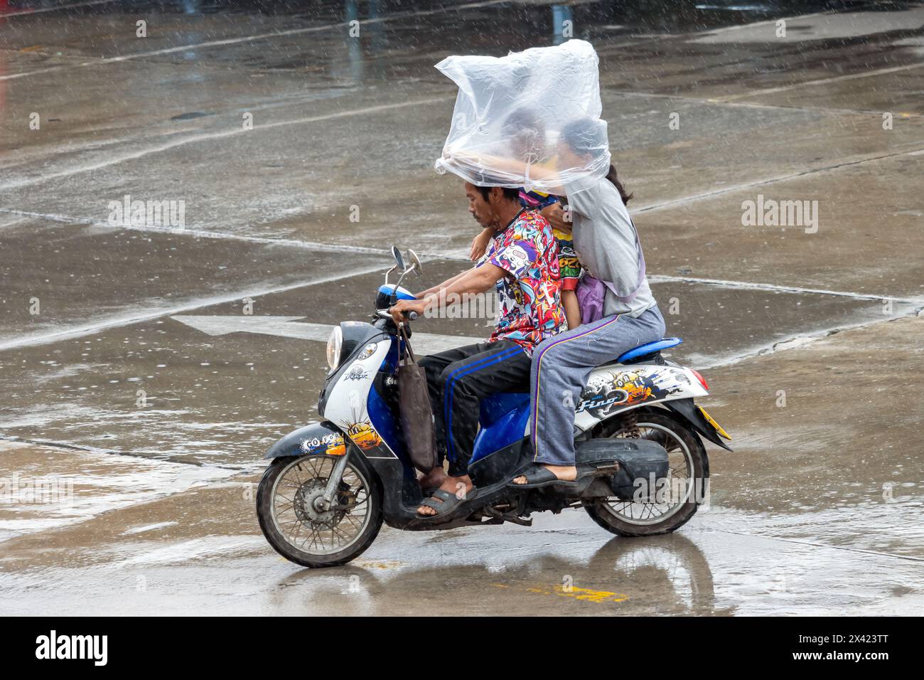 SAMUT PRAKAN, THAILANDIA, 20 Mar 2024, Una famiglia guida una moto sotto la pioggia e si protegge con una grande borsa di plastica Foto Stock