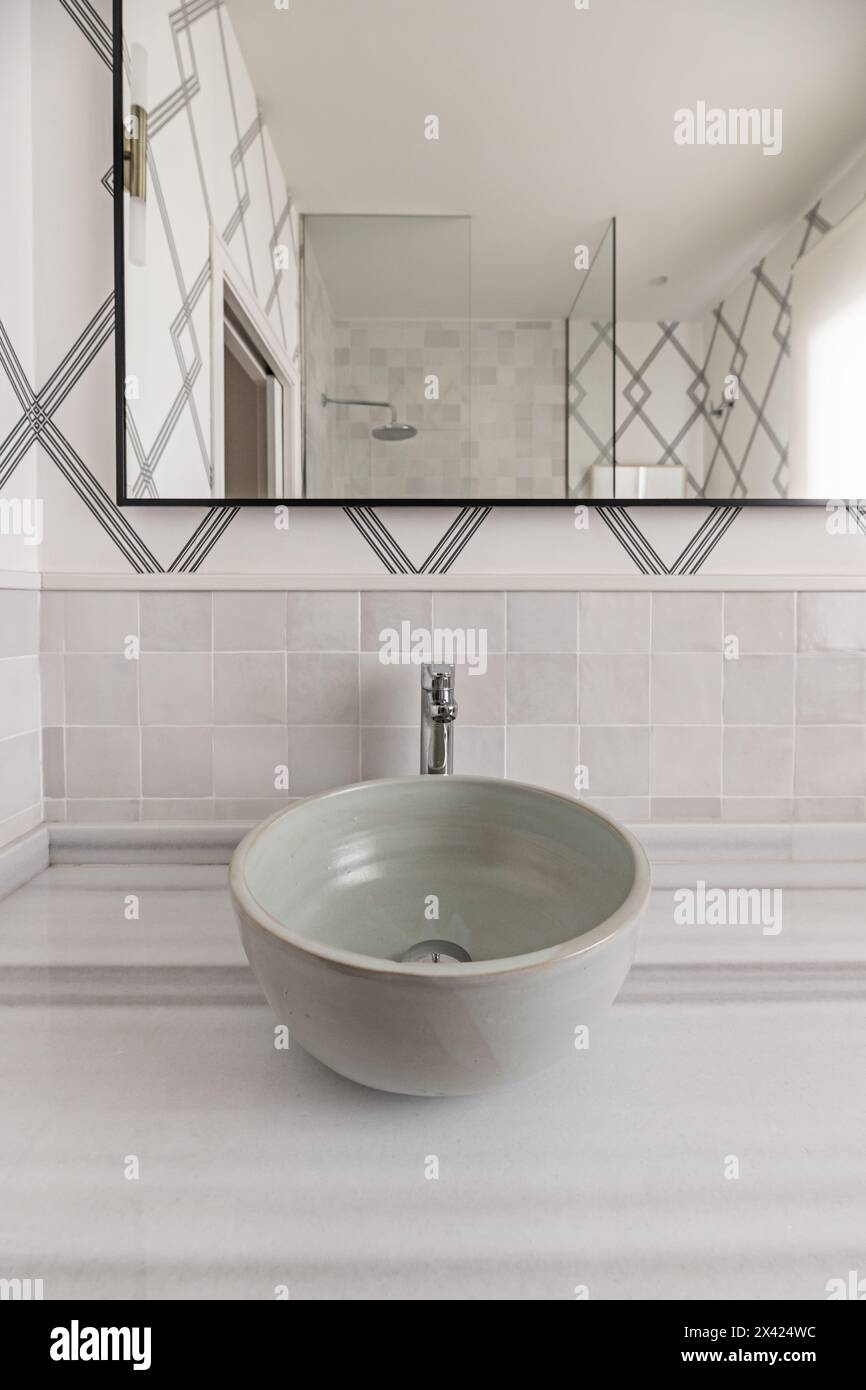 Bagno con lavabo singolo cotto al forno in terracotta, non incorporato in un ripiano in marmo, carta decorativa sulle pareti e uno specchio con un metallo nero Foto Stock