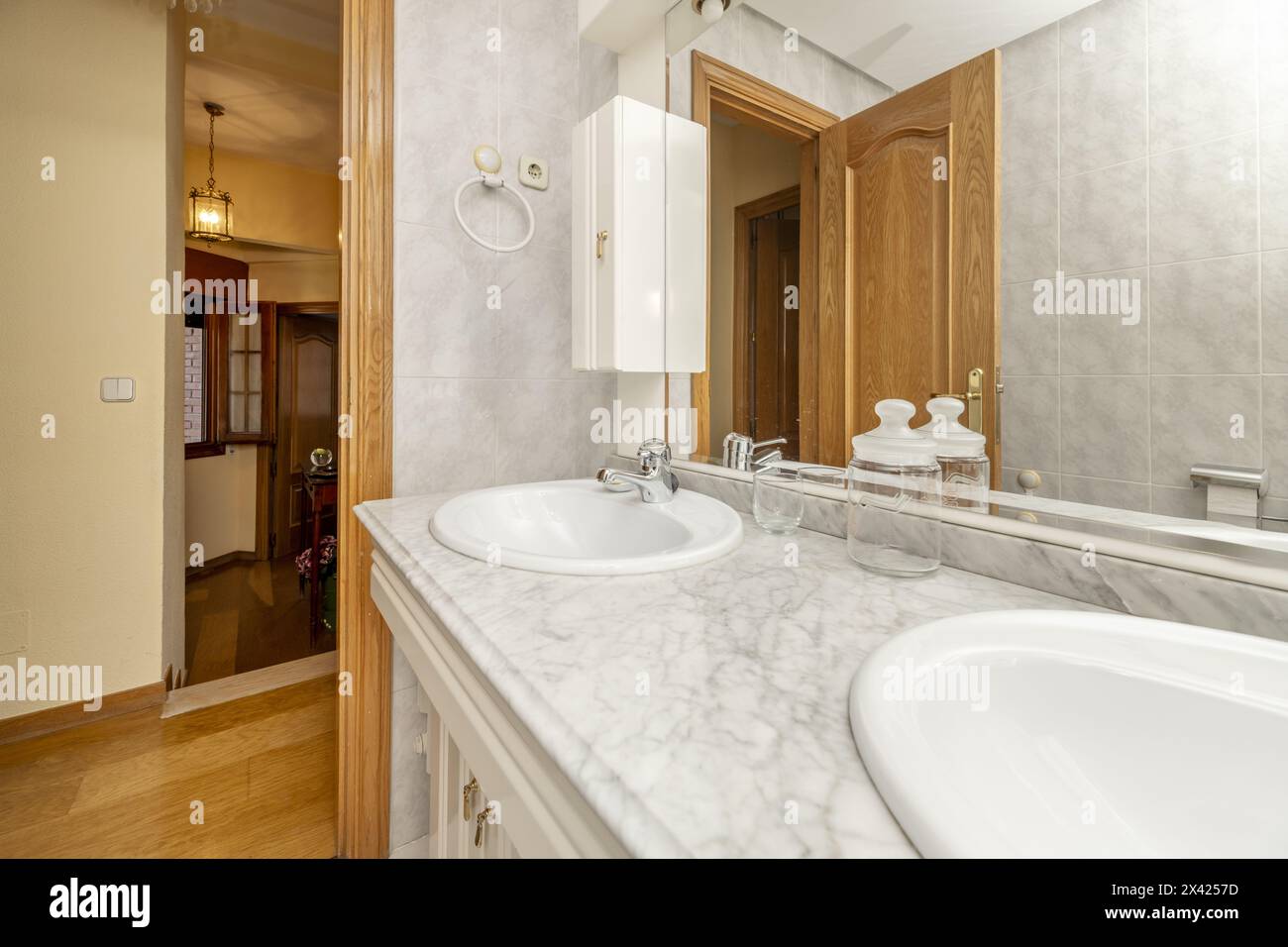 Bagno con due lavandini integrati nel ripiano in marmo e specchio integrato nel mobile in legno bianco Foto Stock