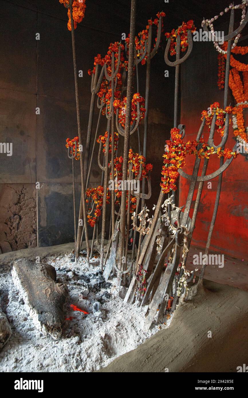 Tridenti di metallo con ghirlande di fiori in una fossa di fuoco in un santuario a Manikarnika Ghat a Varanasi, India. Foto Stock