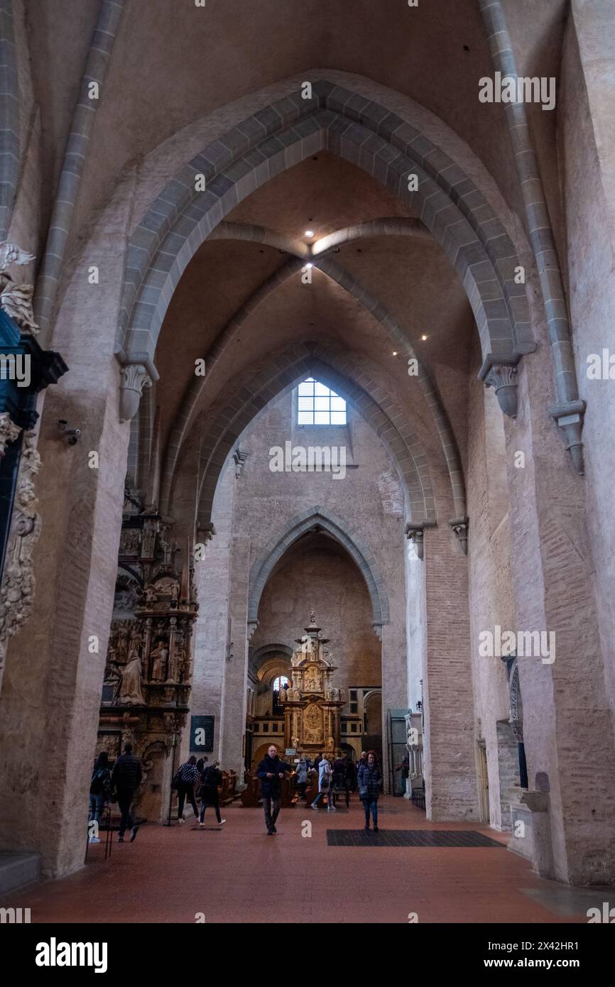 Treviri, Rijnland-Palts, Germania, 23 marzo 2024, l'interno della cattedrale di Treviri, un monumento di importanza religiosa, si apre in una mostra di solennità e grandezza. La navata si estende verso l'alto, mostrando l'architettura romanica della cattedrale con elementi di design gotico. I visitatori sono macchiati ovunque, offrendo un senso di scala e riverenza mentre guardano l'intricata pala d'altare e il gioco di luce attraverso le finestre. Solenne interno della cattedrale di Treviri con i visitatori. Foto di alta qualità Foto Stock