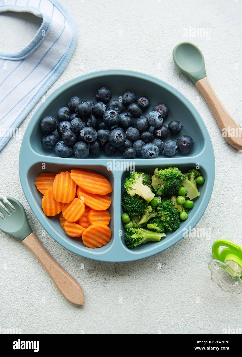 Ciotola in plastica per bambini con broccoli, mirtilli e carote. Alimenti sani per bambini nel recipiente Foto Stock