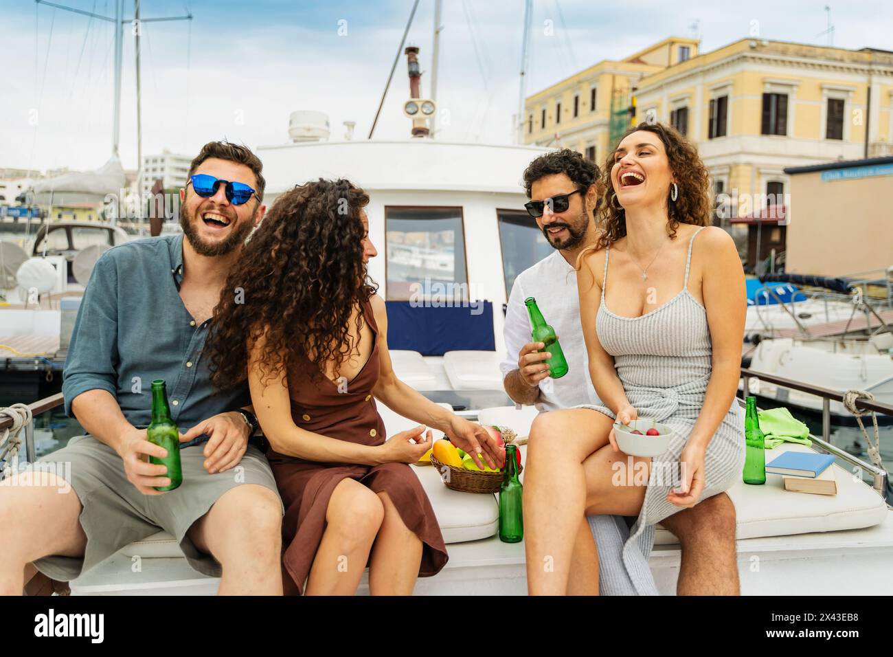 Due coppie felici condividono risate e bevande durante una festa informale in yacht, che incarna il divertimento estivo spensierato al porticciolo. Foto Stock