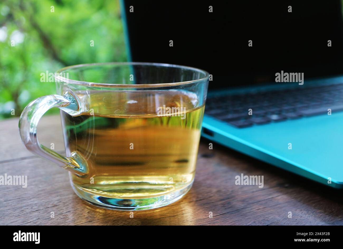 Primo piano di un bicchiere di tè caldo con un computer portatile aperto Foto Stock