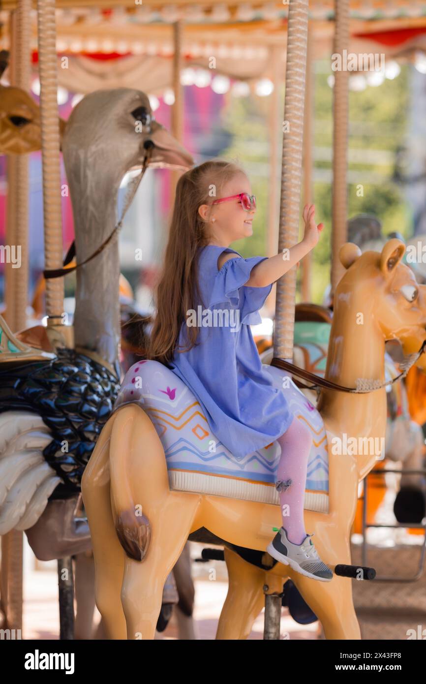 Una bambina felice cavalca una giostra in estate in un parco divertimenti. Foto di alta qualità Foto Stock