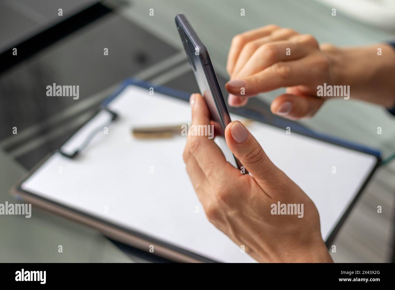 Primo piano della donna con belle mani seduta nella sala riunioni durante una riunione d'affari, usando il suo telefono Foto Stock