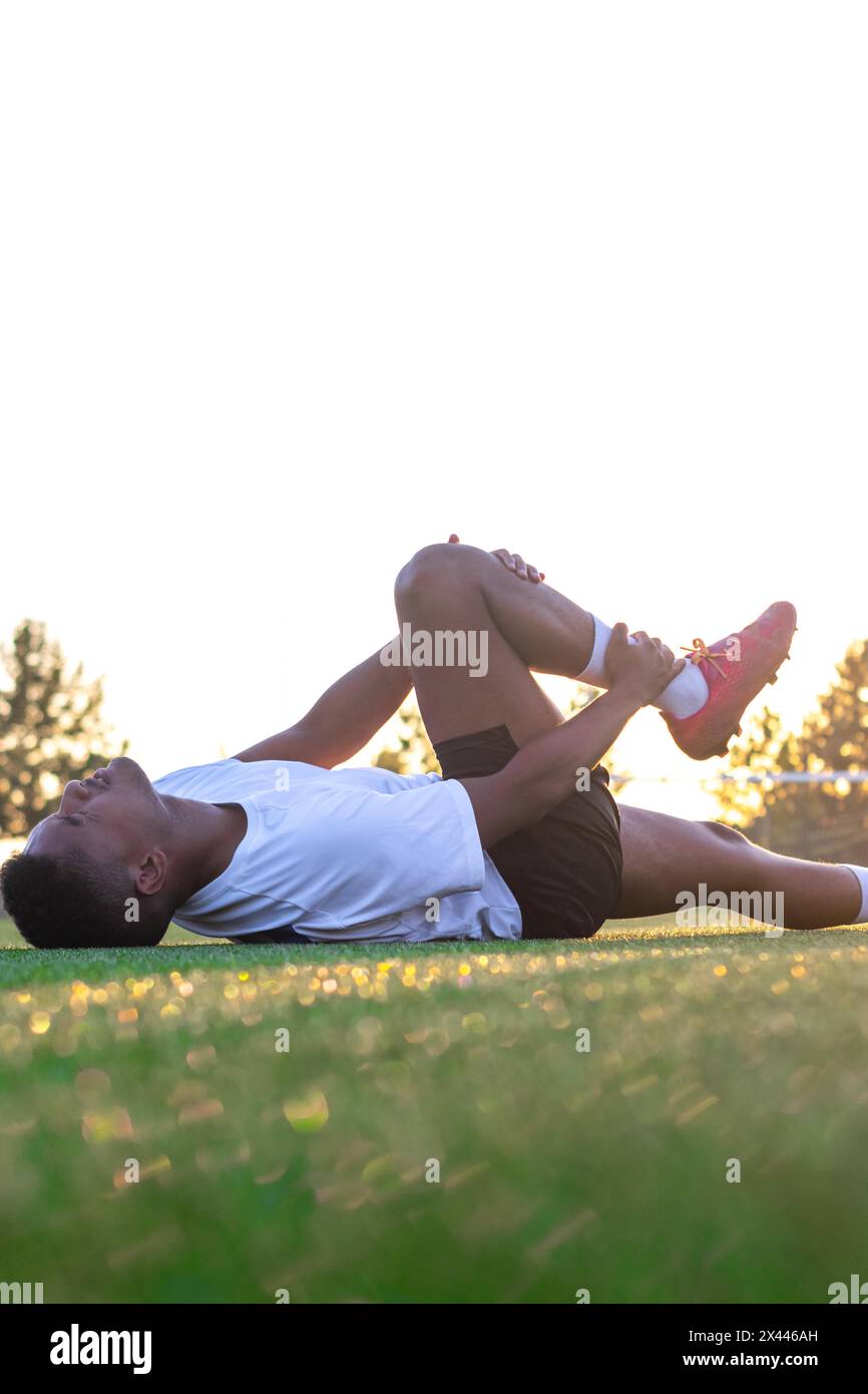Giocatore di football con dolore alle gambe sul campo. Giocatore di calcio steso sull'erba che sfrega la gamba. Giocatore di calcio maschile sdraiato sull'erba che lo sfrega Foto Stock