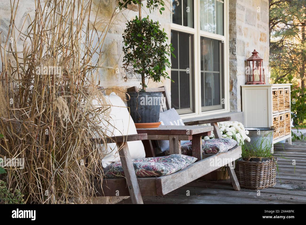 Panca in legno con cuscini e varie piante, erbe, tra cui piante ornamentali e decorazioni sulla veranda anteriore del paese Foto Stock