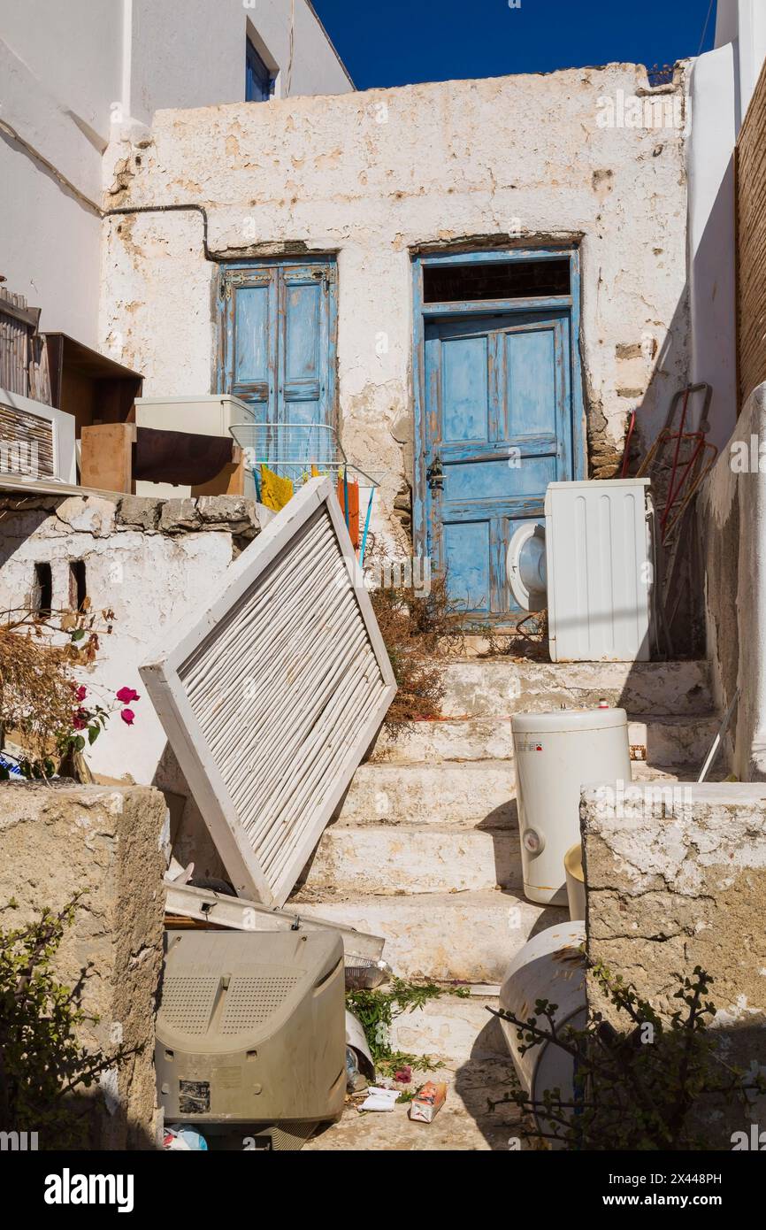 Oggetti scartati nel cortile di casa tradizionale abbandonata con porta d'ingresso in legno blu, città di Mykonos, isola di Mykonos, Grecia Foto Stock