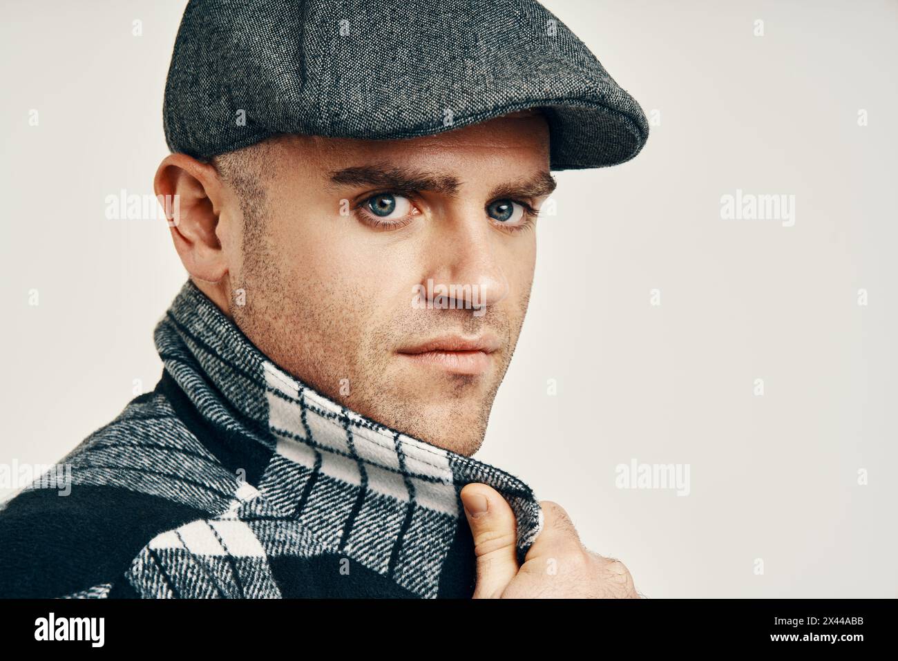 Uomo alla moda con cappello in tweed su morbido sfondo bianco e spazio per le copie. Ispirazione in stile Peaky Blinders Foto Stock