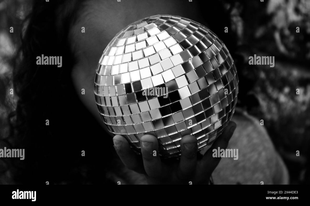 una ragazza che tiene una palla da discoteca davanti alla sua faccia Foto Stock