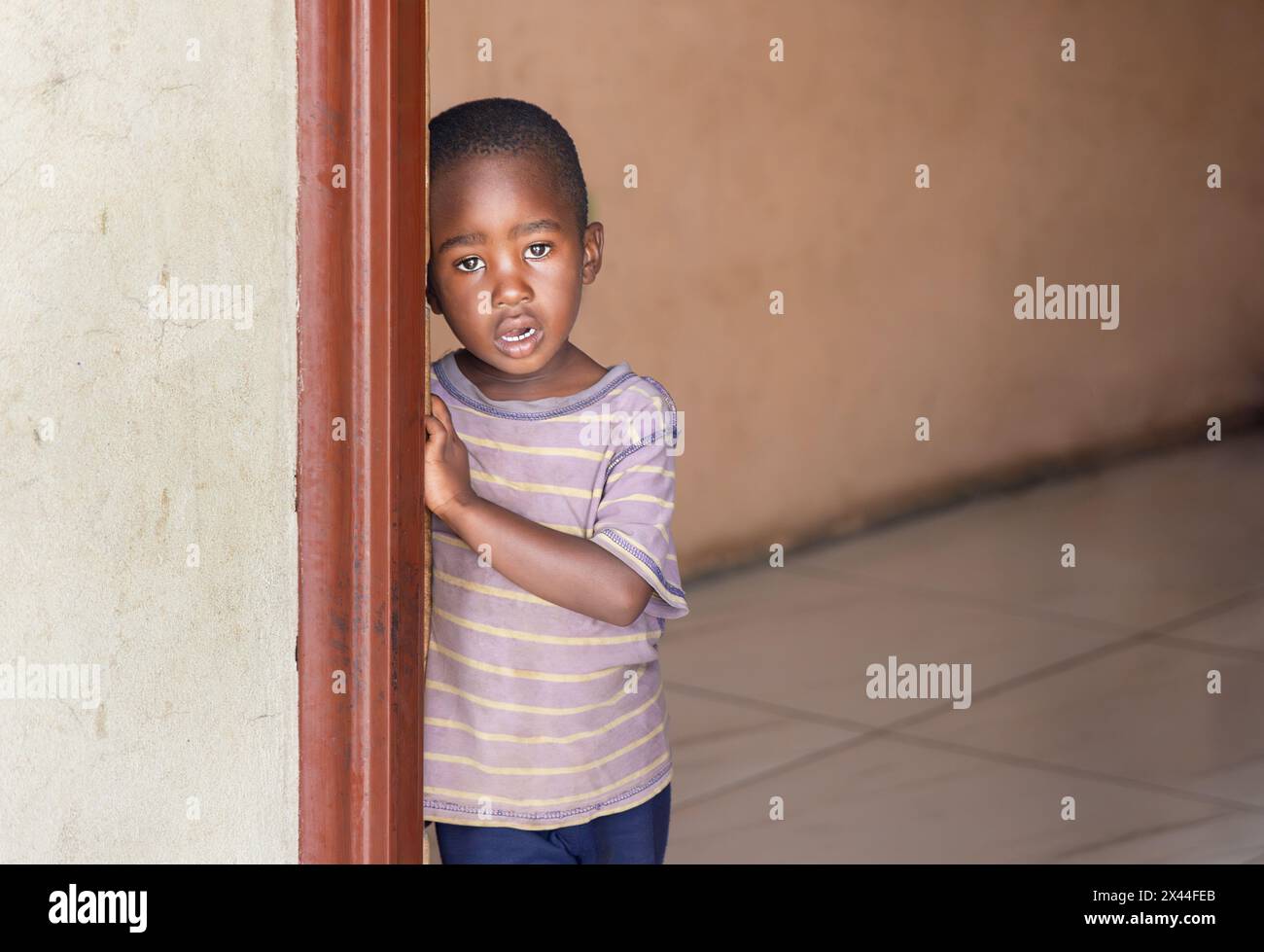 villaggio africano , solitario bambino orfano singolo in una casa vuota, in attesa alla porta, organizzazione di beneficenza ong che organizza genitori adottivi da Foto Stock