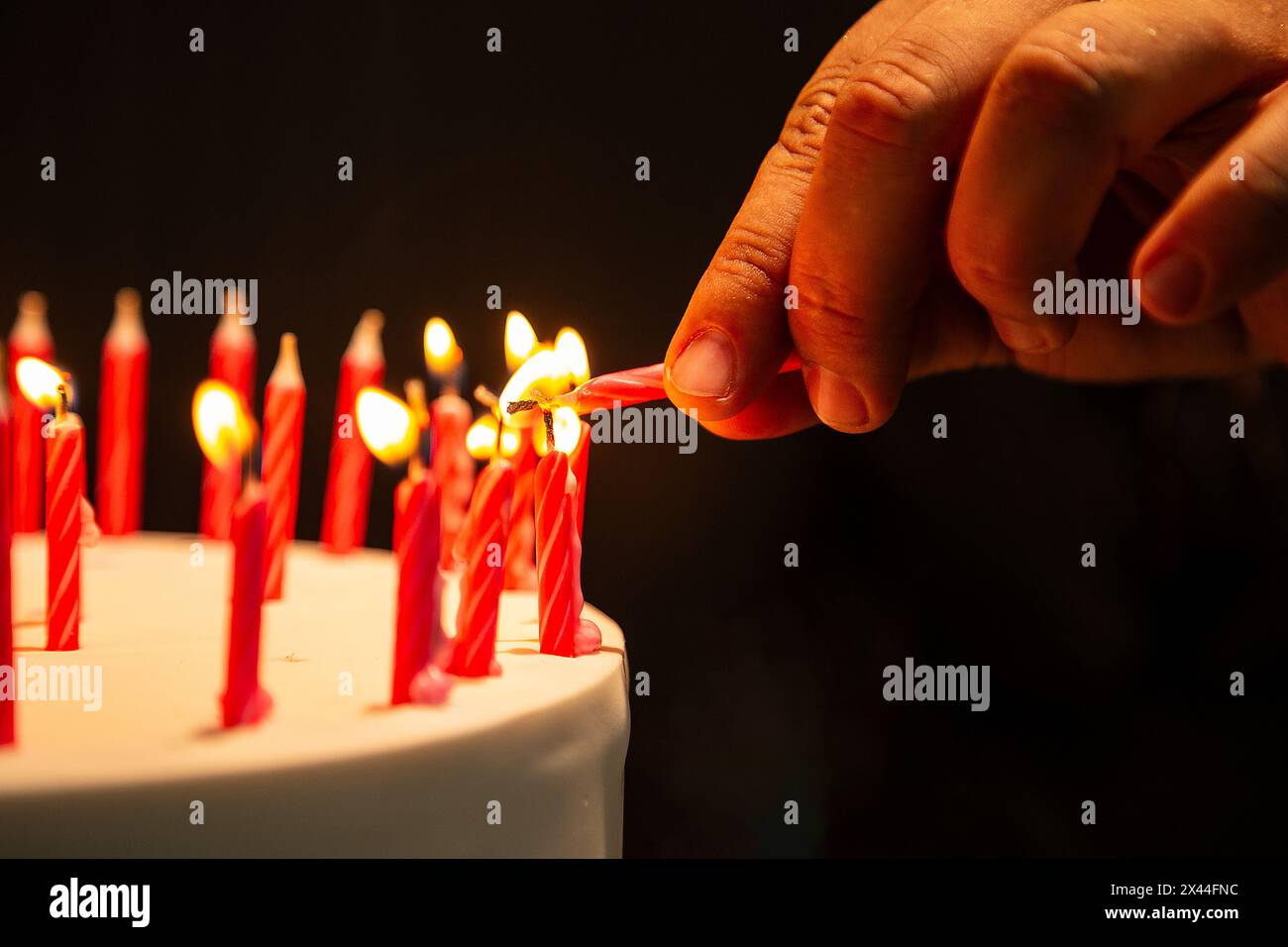 Goiania, Goias, Brasile – 27 aprile 2024: Dettaglio di una mano che accende candele su una torta di compleanno. Messa a fuoco ristretta. Foto Stock