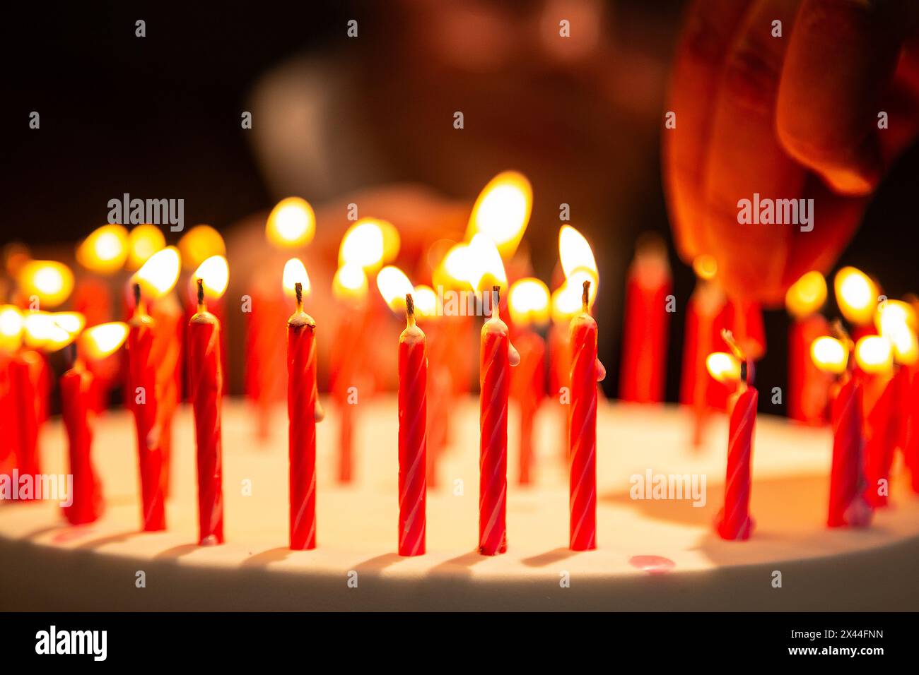 Goiania, Goias, Brasile – 27 aprile 2024: Dettaglio di una mano che mette una candela e diverse altre candele su una torta di compleanno. Foto Stock