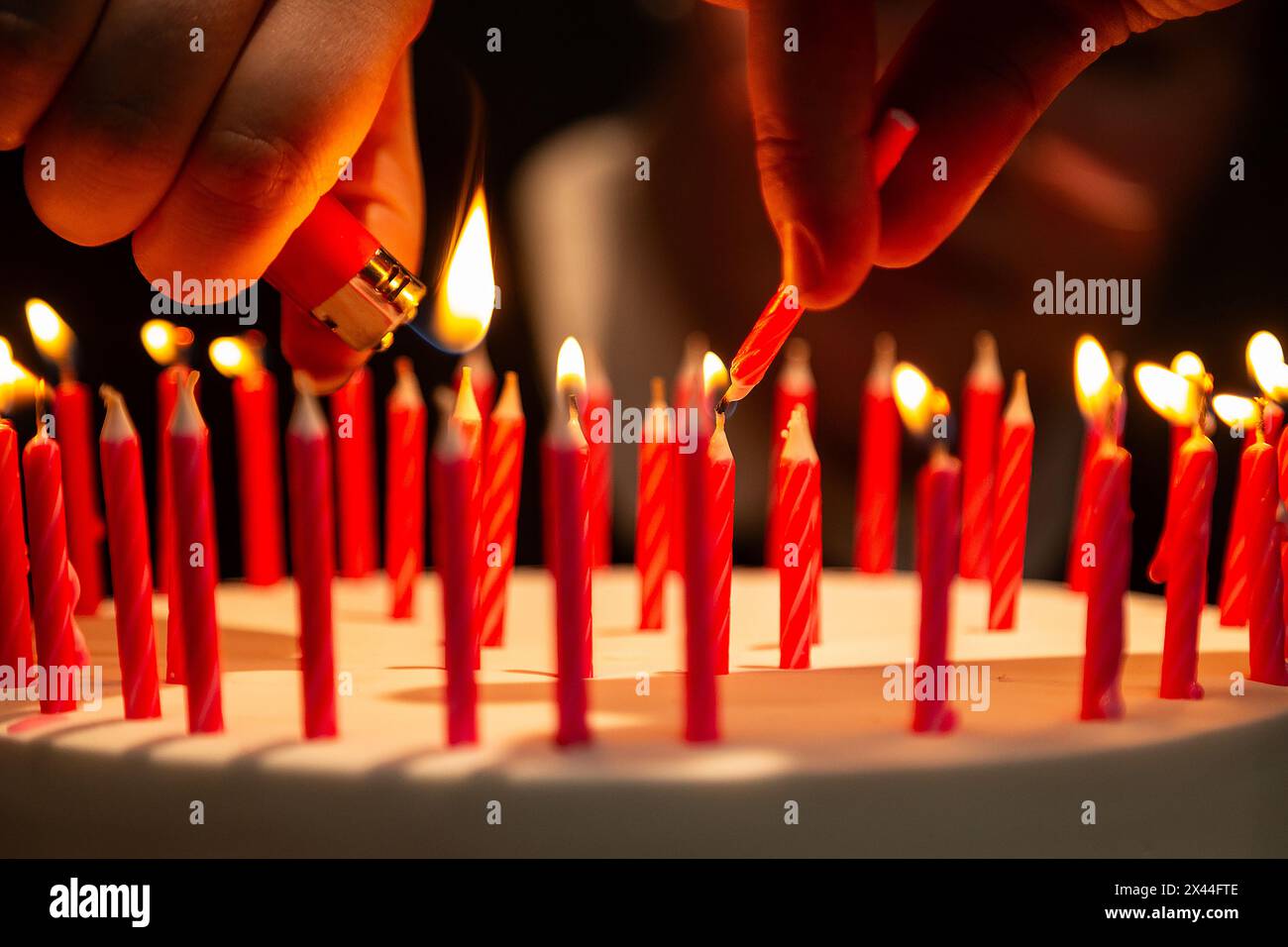 Goiania, Goias, Brasile – 27 aprile 2024: Dettaglio delle mani che illuminano molte candele su una torta di compleanno. Messa a fuoco ristretta. Foto Stock