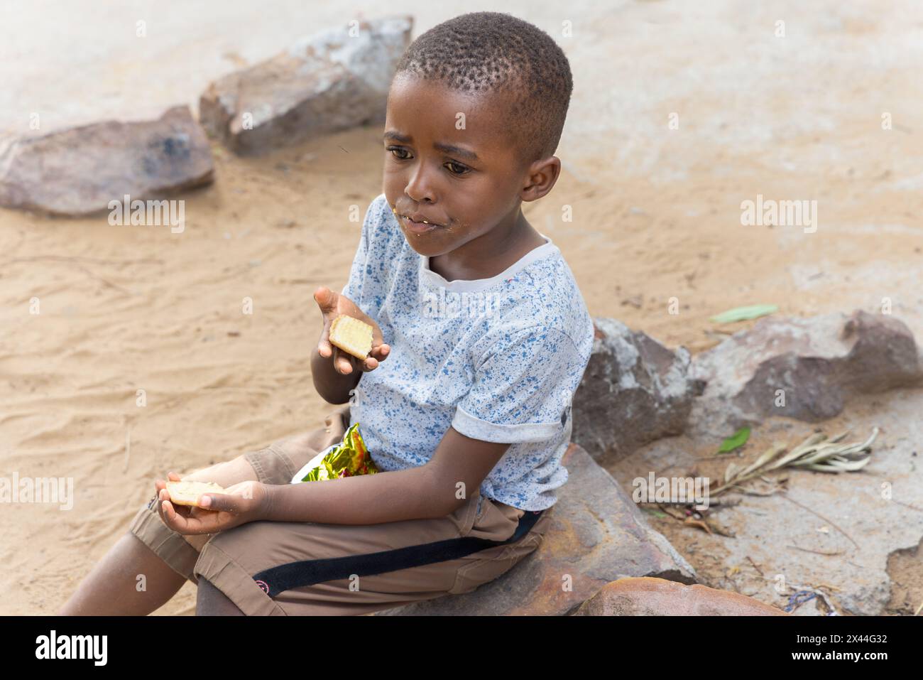 villaggio africano, bambini che mangiano biscotti e spuntini di mais adagiati su una pietra nel cortile Foto Stock