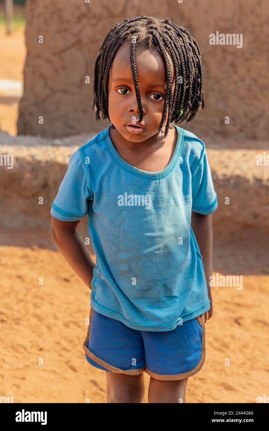 villaggio africano, bambina piccola con trecce di fronte a una casa di fango Foto Stock