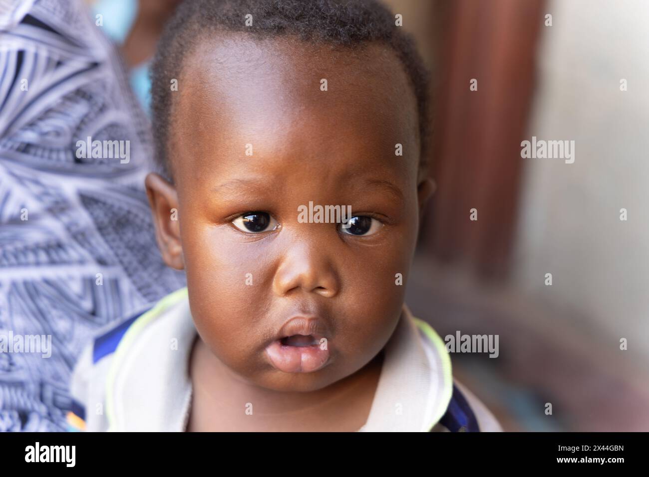 villaggio africano, bambino piccolo di fronte alla casa sul portico, madre sullo sfondo Foto Stock