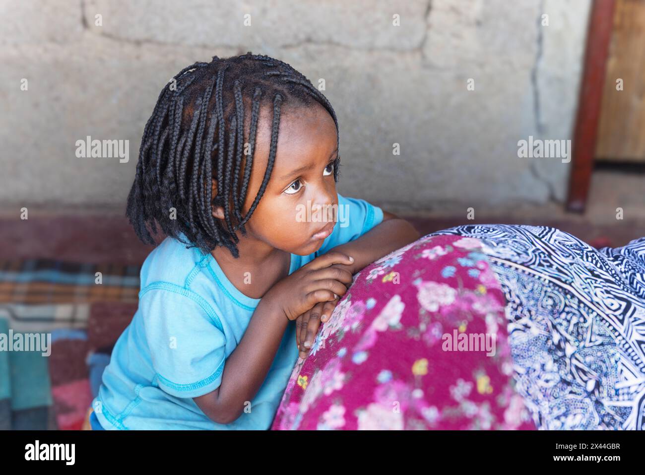 villaggio africano, ragazzina con trecce davanti alla casa sul portico appoggiata alla madre Foto Stock