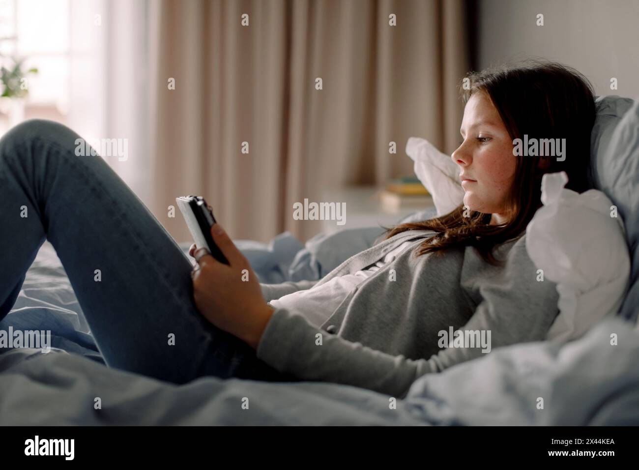 Vista laterale della ragazza adolescente con tablet digitale disteso sul letto di casa Foto Stock