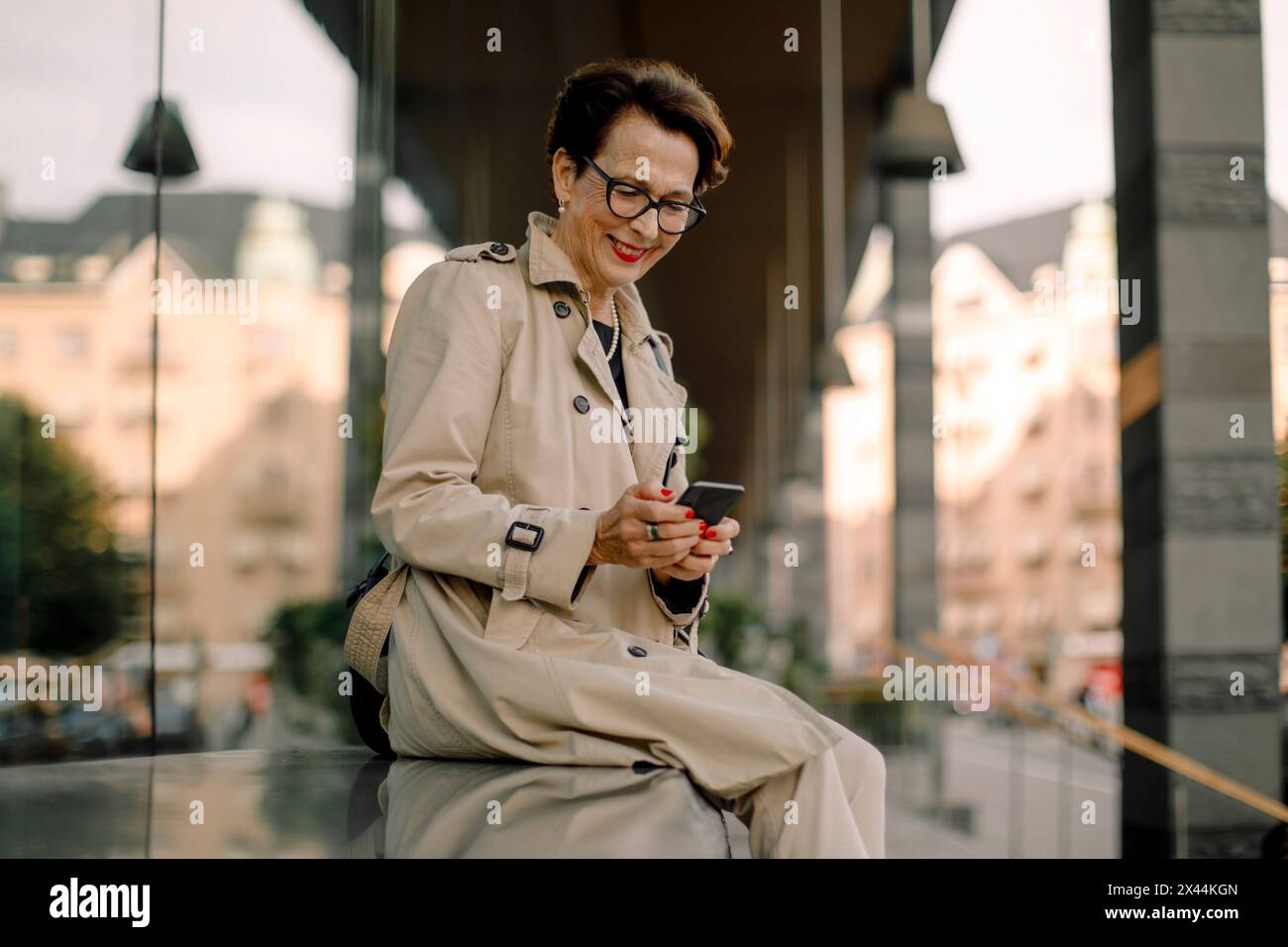 Sorridente donna anziana in pensione che usa lo smartphone mentre è seduta sulla panchina Foto Stock