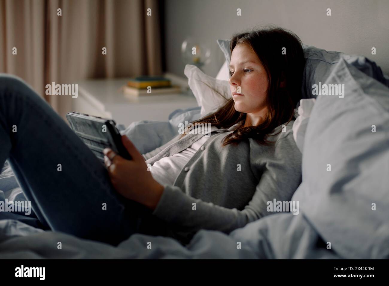 Vista laterale di una ragazza adolescente con tablet digitale sdraiata sul letto della camera da letto di casa Foto Stock