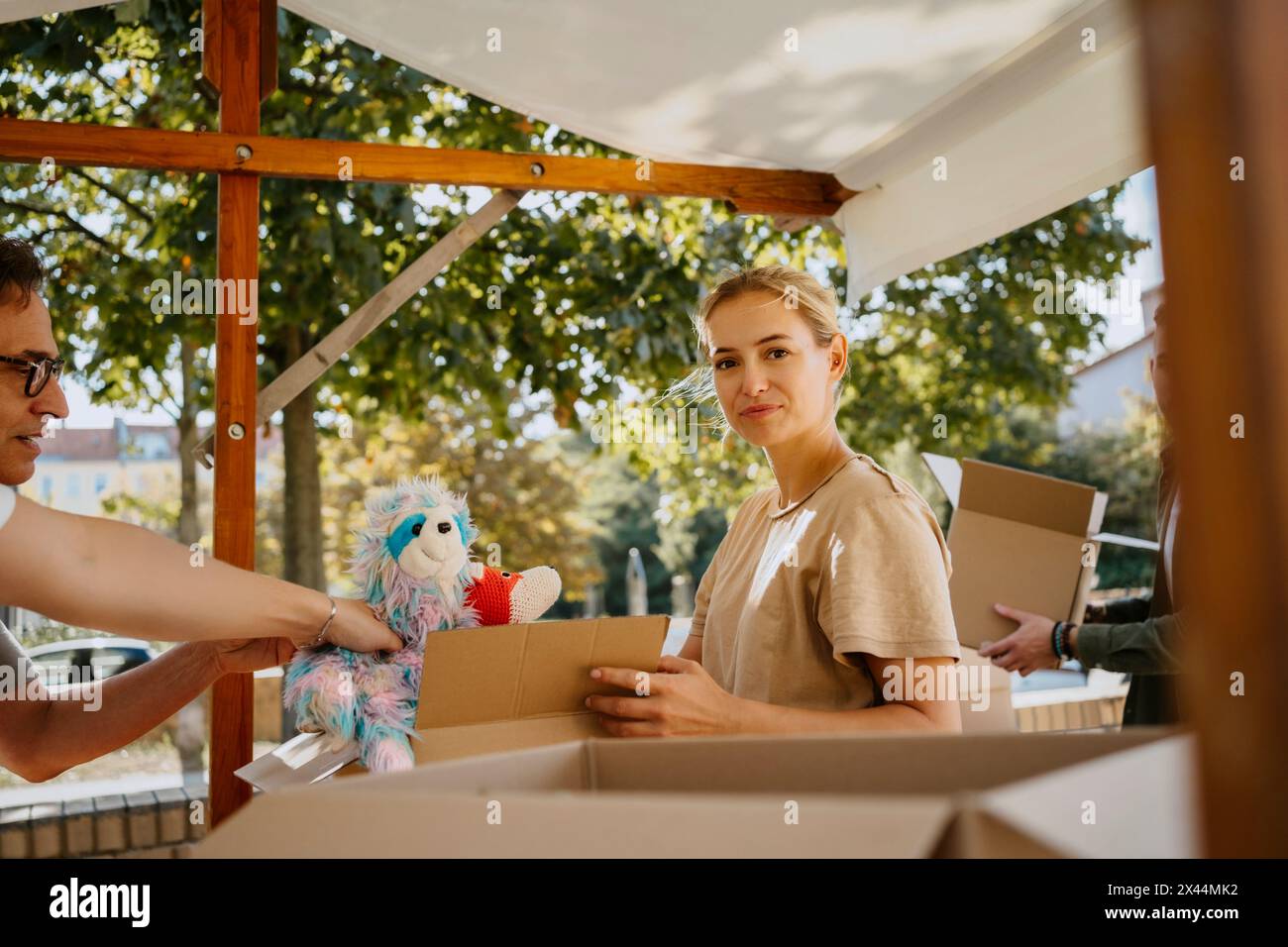 Ritratto di una volontaria sorridente che confeziona giocattoli imbottiti in scatole con i colleghi del centro della comunità Foto Stock