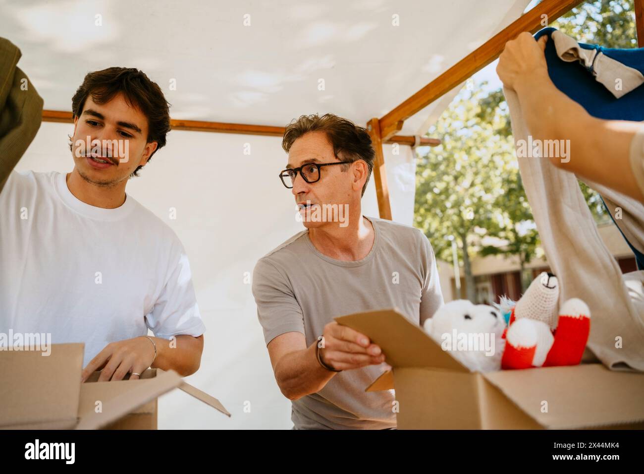 Giovane volontario che discute con un collega maschio anziano mentre cercava vestiti e giocattoli imbottiti in scatole presso il centro della comunità Foto Stock