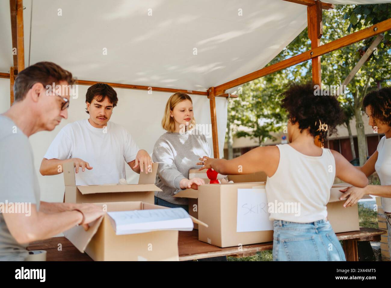 Gruppo di volontari multirazziali che selezionano le casse di donazione sotto la tenda durante un viaggio di beneficenza presso il centro della comunità Foto Stock