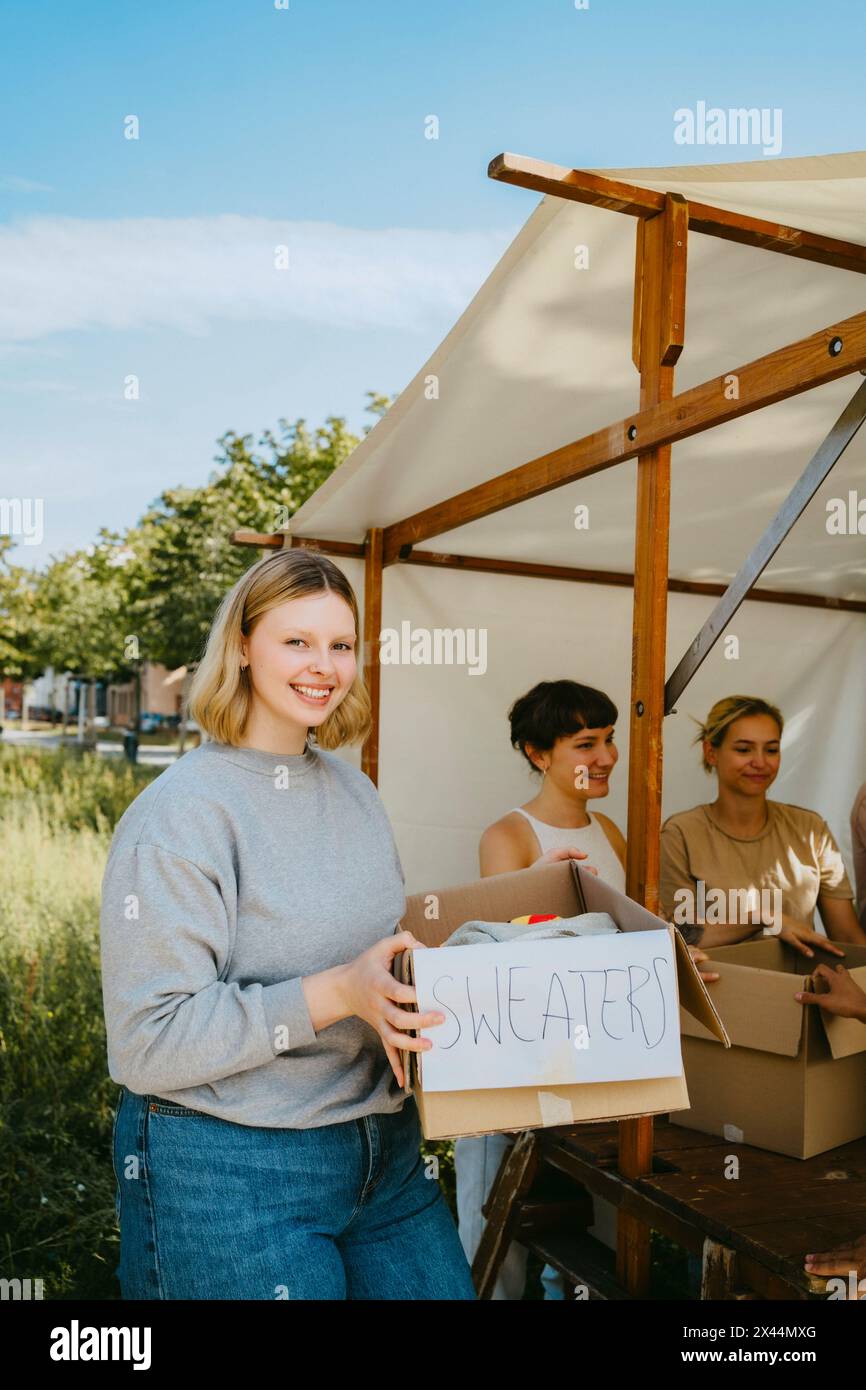 Ritratto di un volontario felice che tiene in mano una scatola maglione durante un viaggio di beneficenza al centro della comunità Foto Stock