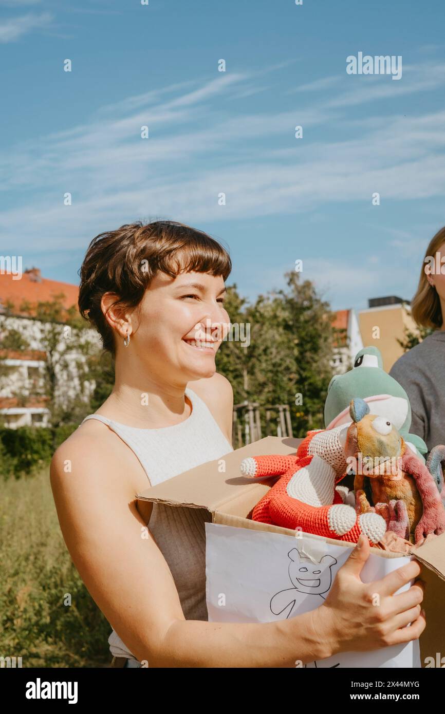 Volontaria felice che tiene in mano una scatola con giocattoli imbottiti durante un viaggio di beneficenza presso il centro della comunità Foto Stock