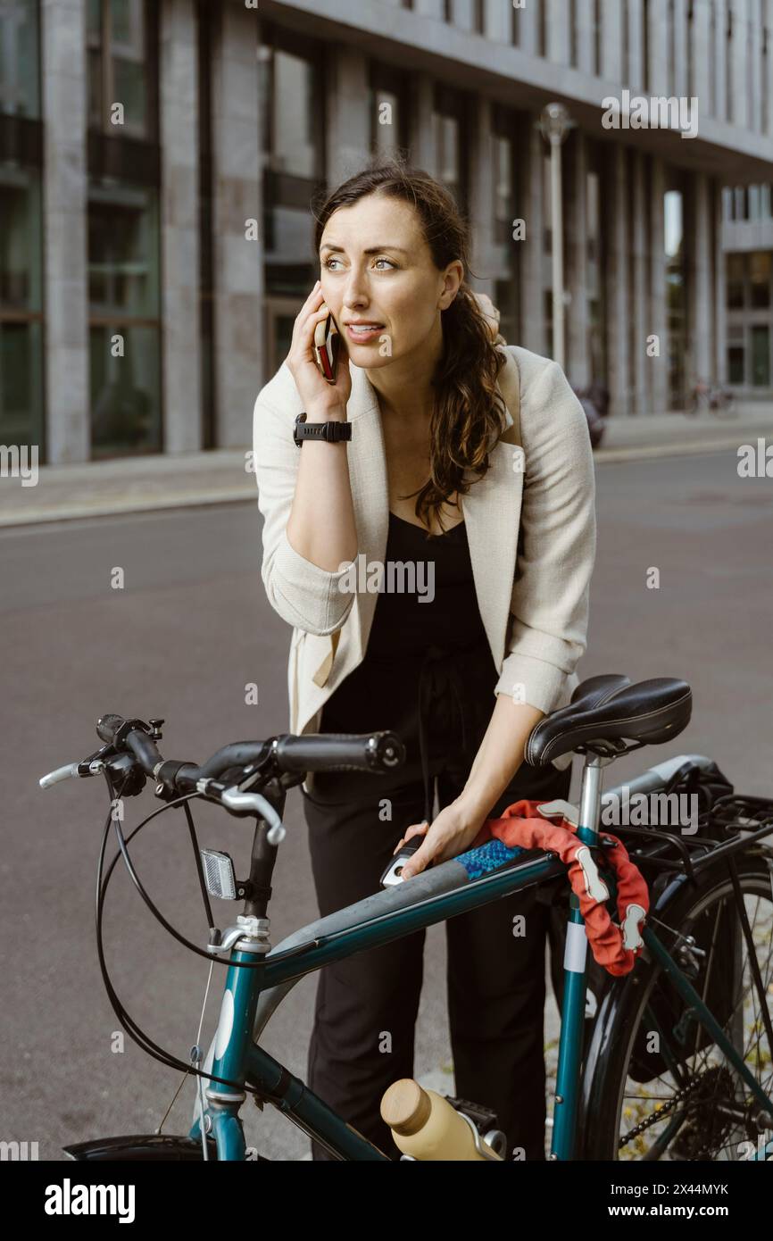 Donna d'affari che blocca la bicicletta mentre parla con uno smartphone in città Foto Stock
