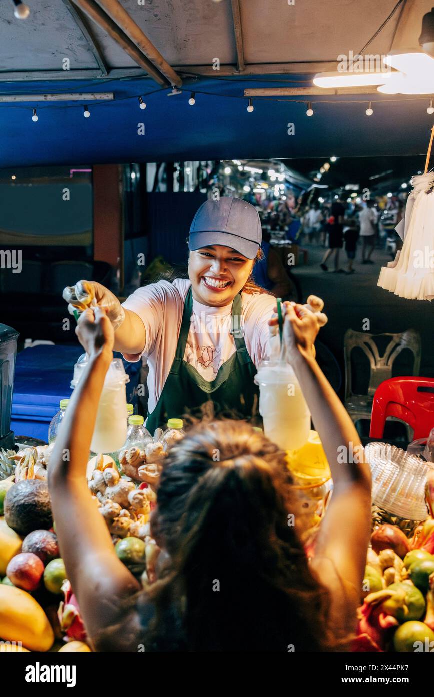 Una donna sorridente che dà bicchieri da succo alla ragazza al mercato alimentare Foto Stock