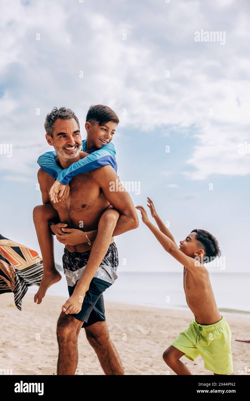 Uomo senza camicia che fa il piggyback figlio in spiaggia contro il cielo Foto Stock