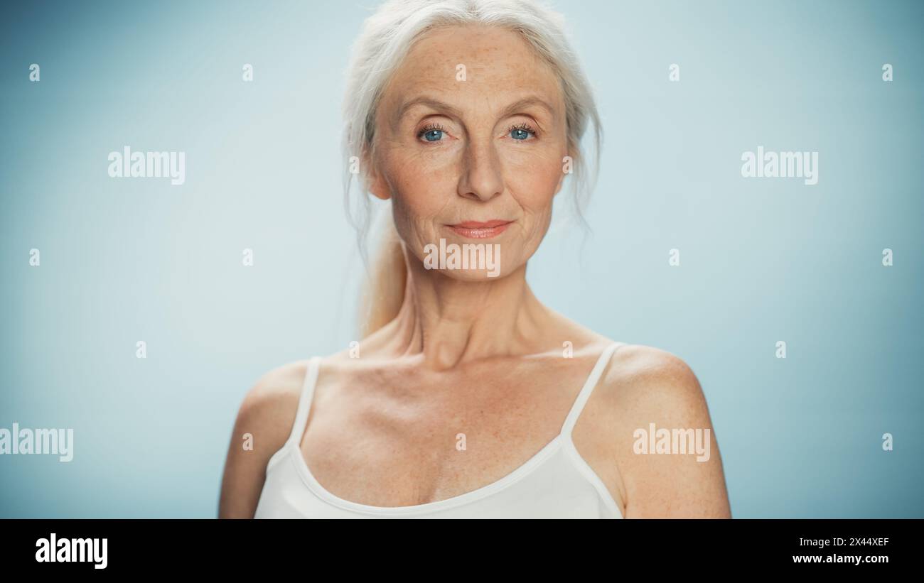 Ritratto di una bella donna anziana che guarda la fotocamera e sorride meravigliosamente. Signora anziana con capelli grigi naturali, occhi blu, con Top. Bellezza e dignità della vecchiaia Foto Stock