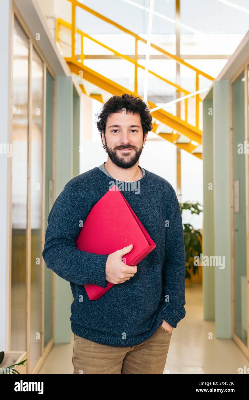 Ritratto di un uomo bianco sorridente in un coworking che tiene una cartella Foto Stock