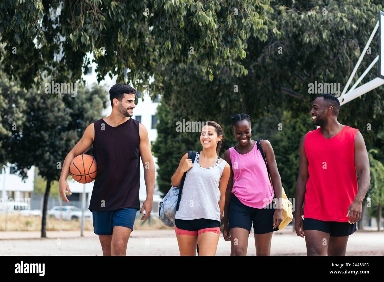 Un gruppo di amici interrazziali in abbigliamento sportivo mentre si recano a giocare a basket sul campo Foto Stock