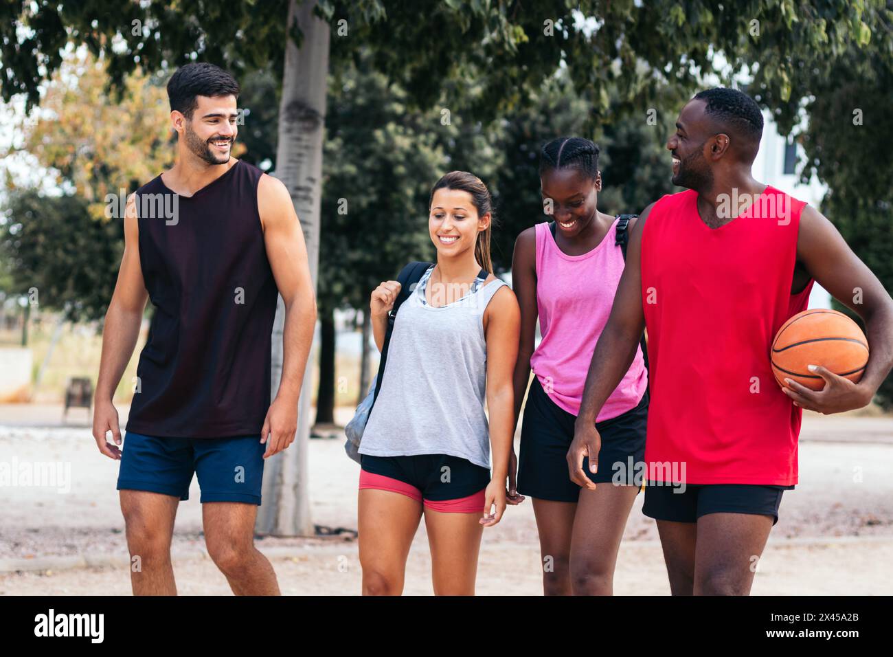 Un gruppo di amici interrazziali in abbigliamento sportivo mentre si recano a giocare a basket sul campo Foto Stock