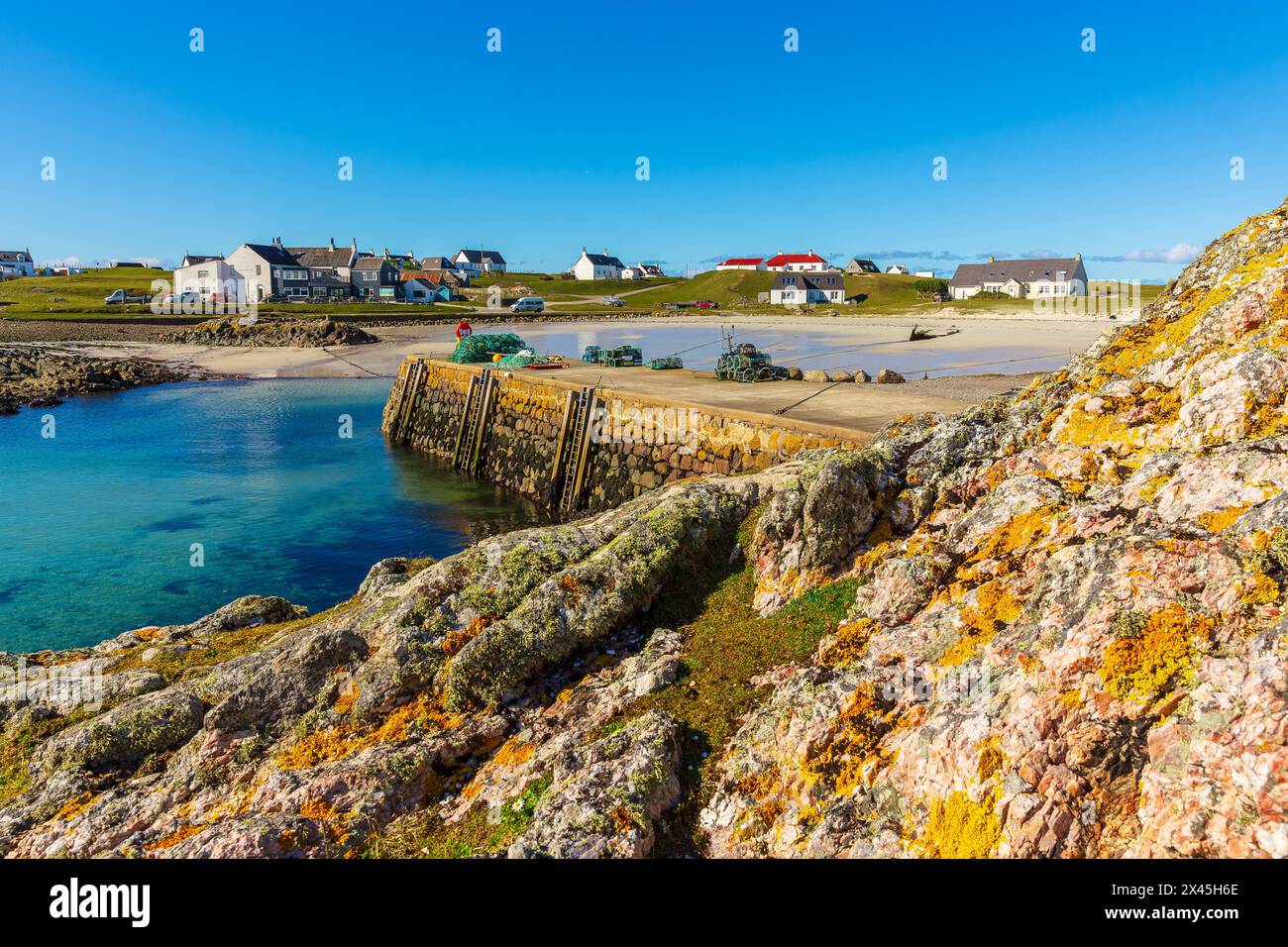 Scarinish, Tiree, Scozia, marzo 26 2024 il bellissimo villaggio, porto e molo di Scarinish sull'isola ebridea di Tiree, Scozia con la blu S. Foto Stock