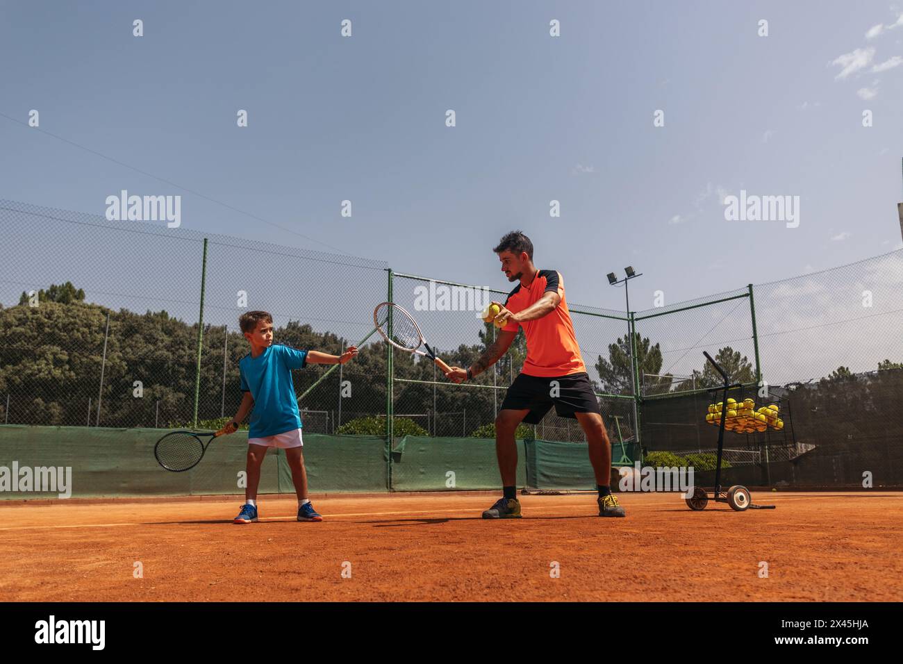 Uomo che allena un bambino a tennis, insegnandogli movimenti e posture in modo che il bambino sia il migliore. Foto Stock