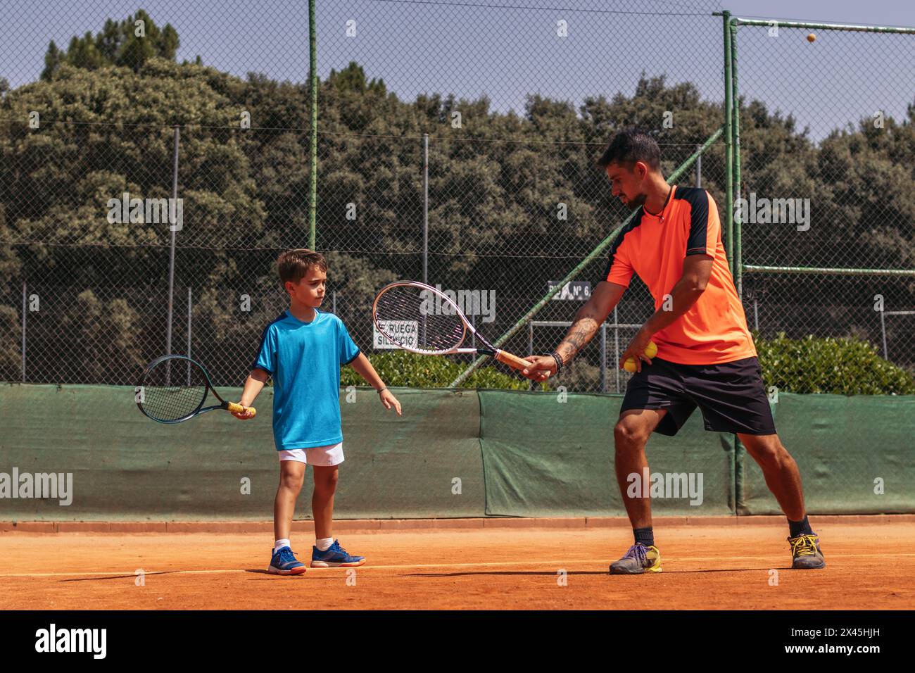 Uomo che allena un bambino a tennis, insegnandogli movimenti e posture in modo che il bambino sia il migliore. Foto Stock