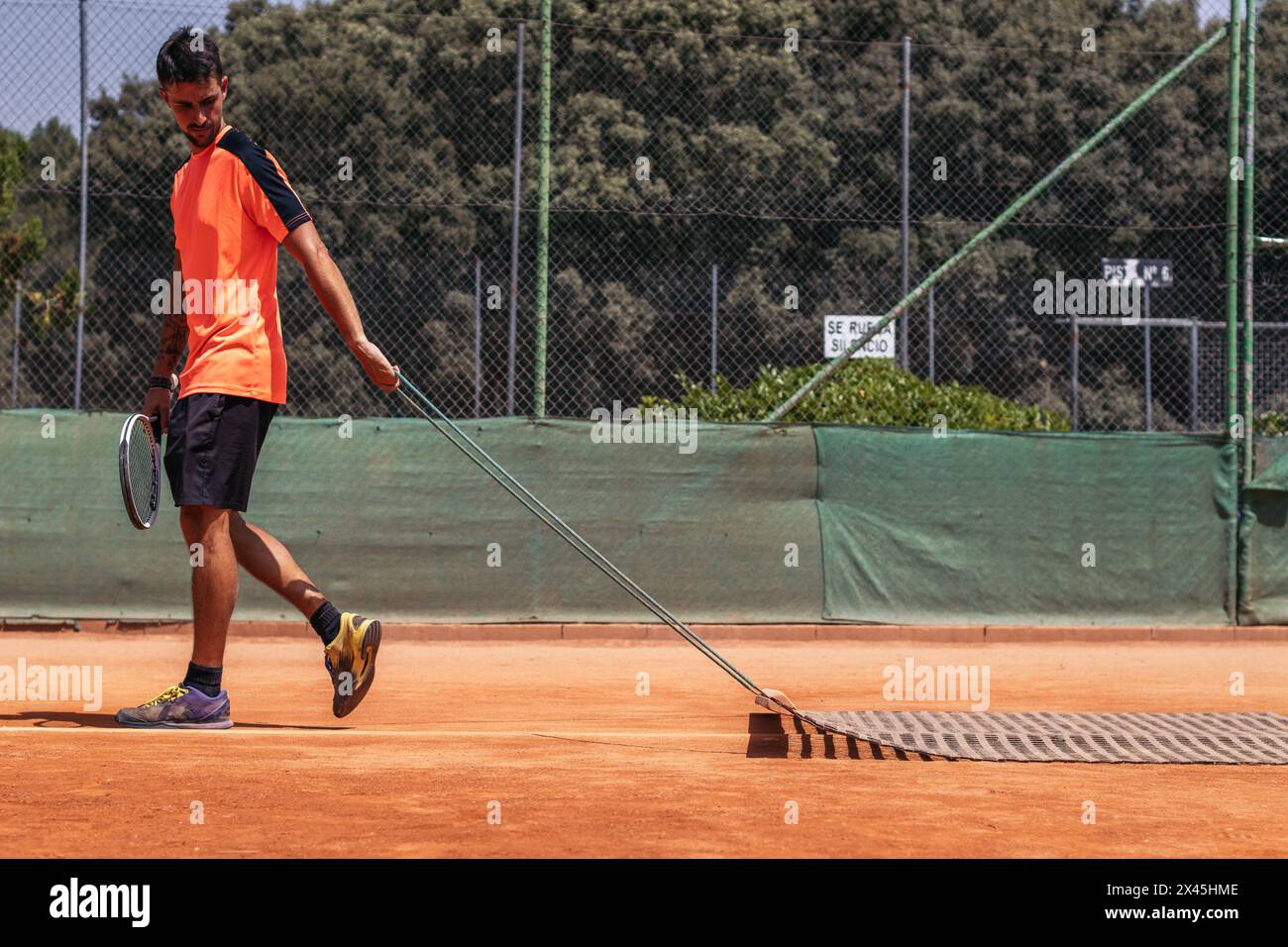 Uomo in abbigliamento sportivo che posa il tennis su un campo da tennis in terra battuta. Passa il tappeto per pavimentare la corte Foto Stock
