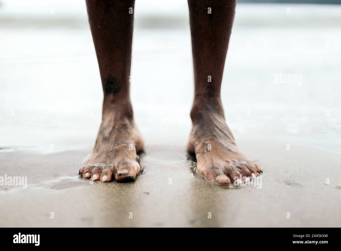 Primo piano di piedi sulla sabbia sulla spiaggia. Piedi tatuati di un uomo afroamericano Foto Stock