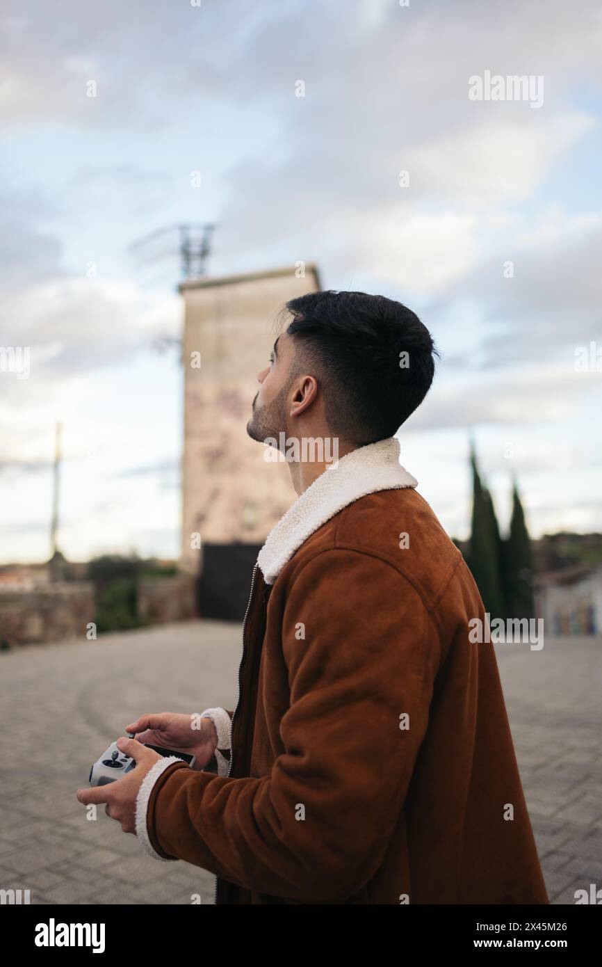 Giovane uomo che usa un drone per fotografare e registrare il paesaggio. Controlla il drone con il controller mentre guarda il cielo guardando il dr Foto Stock