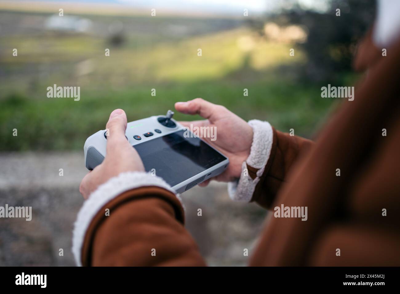 Primo piano delle mani del pilota di un drone che tiene in mano un controller con uno schermo mentre si aziona il drone. Foto Stock