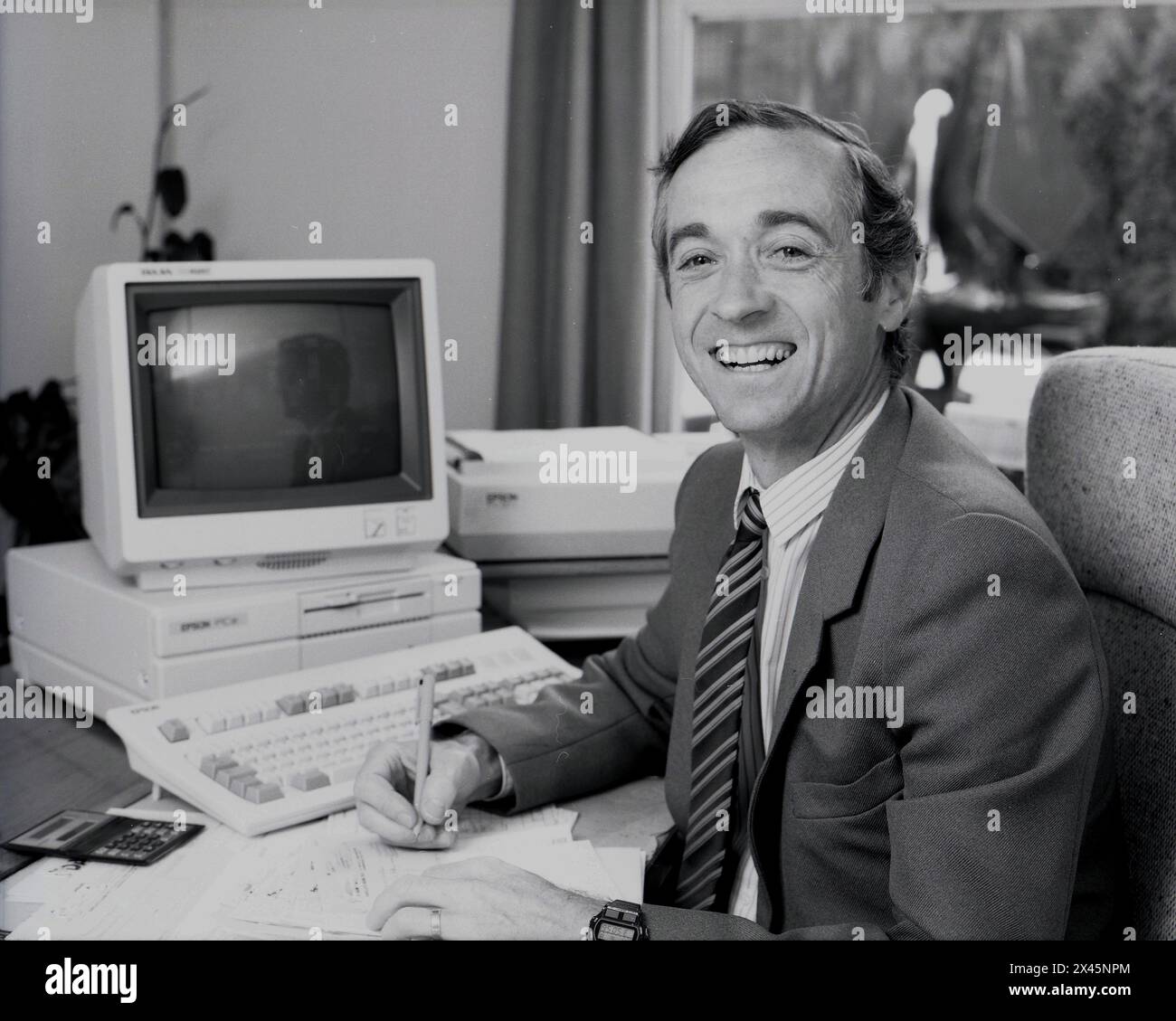 1987, un dirigente d'affari maschile alla sua scrivania, un contabile, che scrive un assegno. Un monitor di computer dell'epoca, un VT320 digitale accanto a lui. Il VT320 era un popolare terminale informatico in questa epoca per l'elaborazione dei dati, comunemente usato nelle biblioteche per la catalogazione dei libri. Foto Stock