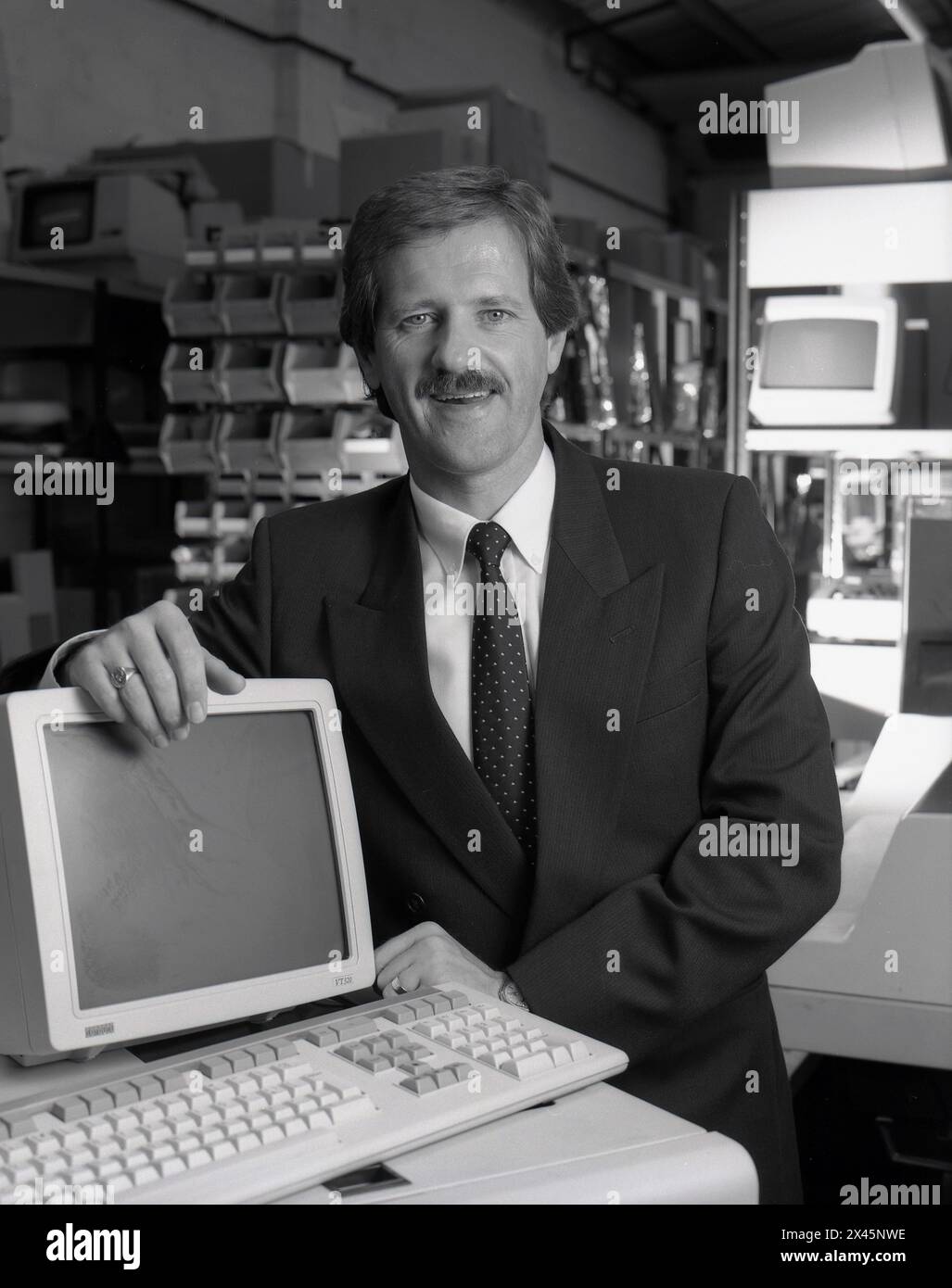 1987, un venditore di computer in tuta e cravatta accanto a un terminale di computer dell'epoca, un VT320 digitale, prodotto dalla Digital Equipment Corporation (DEC). Il VT320 era un monitor di solo testo, comunemente usato nelle librerie per i dati e la catalogazione. Foto Stock